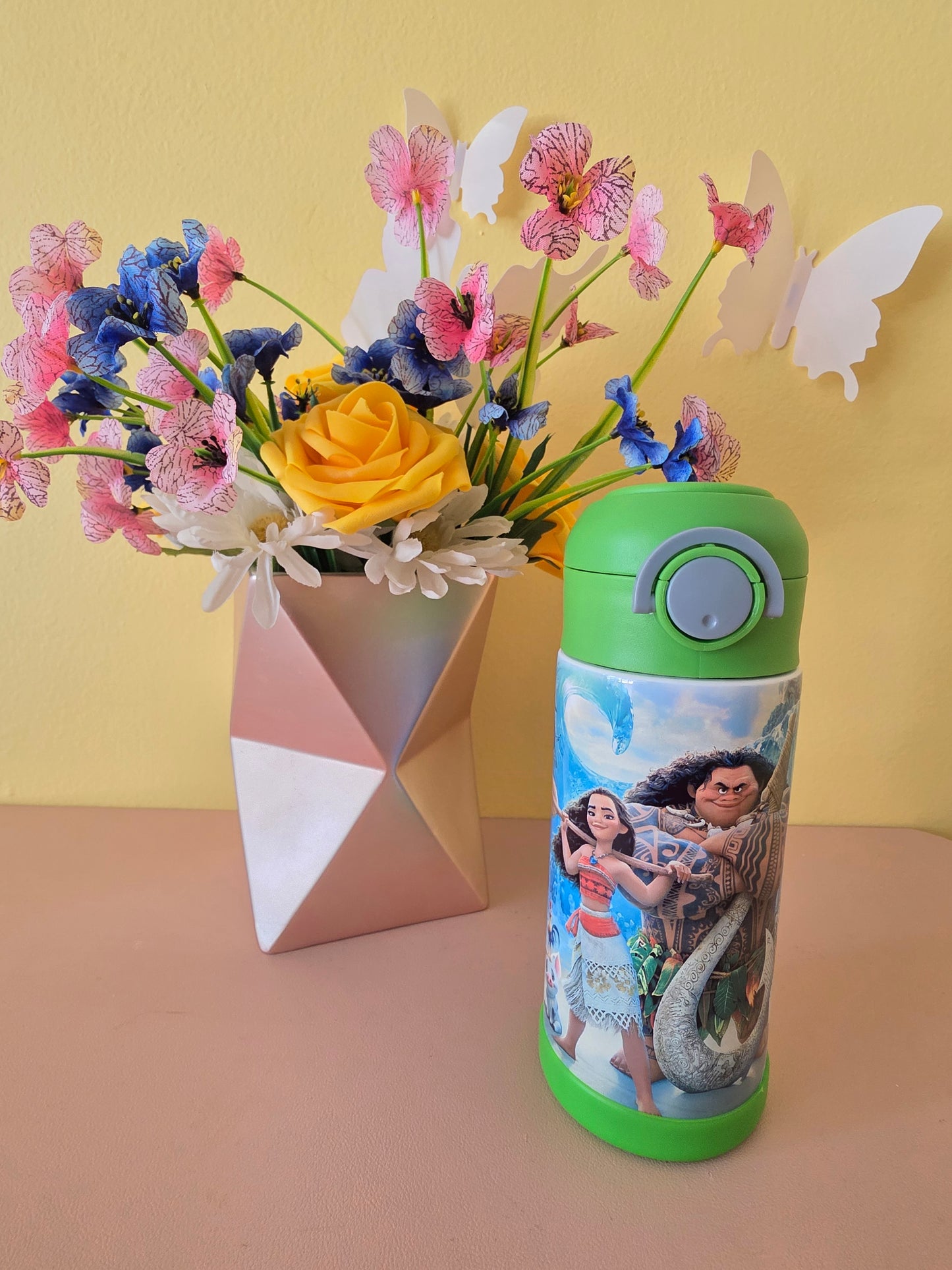 Moana and Maui Tumbler on a table with flowers in the background. 