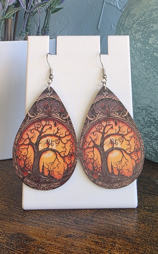 Teardrop-shaped earrings with tree design on a white stand.