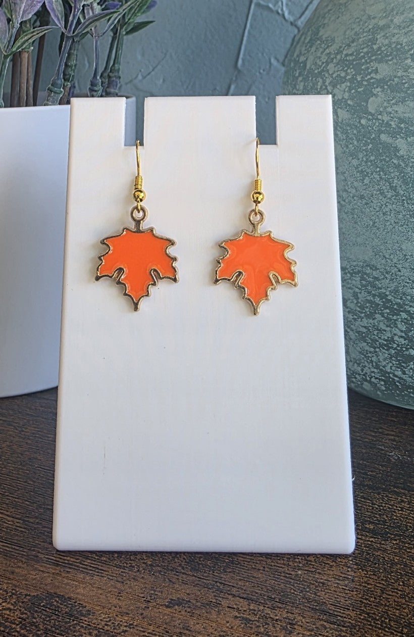Orange leaf-shaped earrings on a white stand with a blurred background