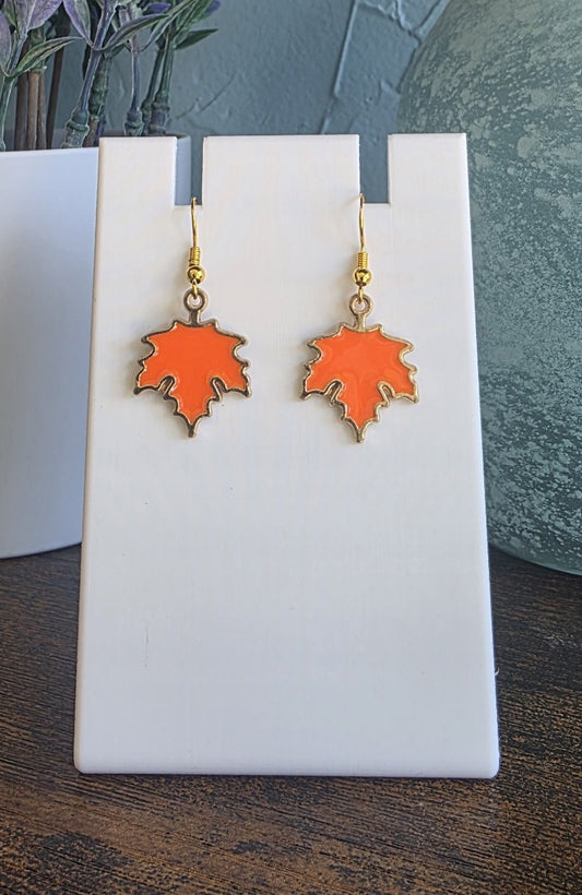 Orange leaf-shaped earrings on a white stand with a blurred background