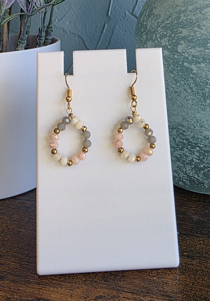 Pair of hoop earrings with beads on a white stand with a blurred background
