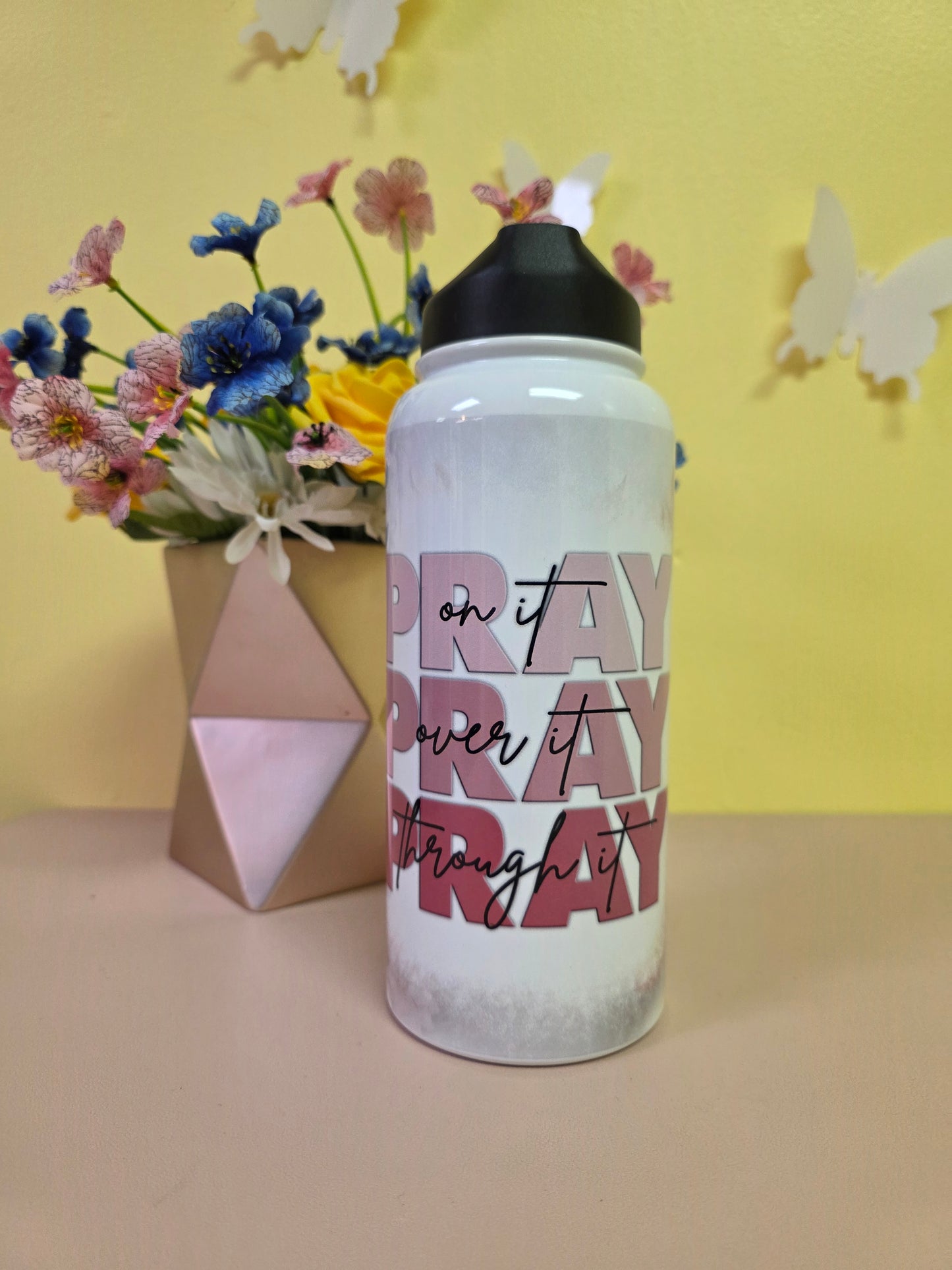 Water bottle with a prayer design on a table with yellow background. 