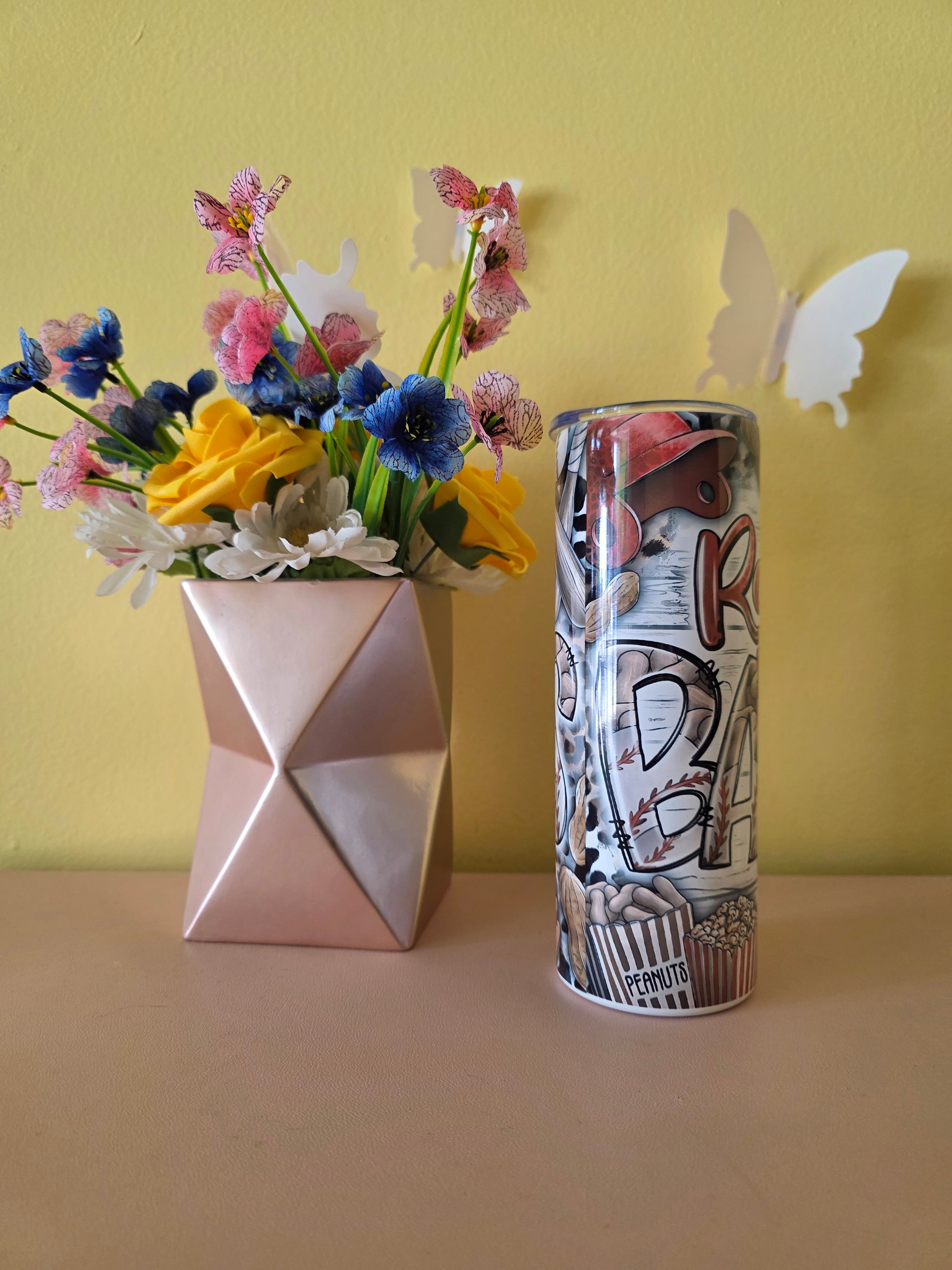 Decorative tumbler with colorful baseball design on a pink surface and yellow background