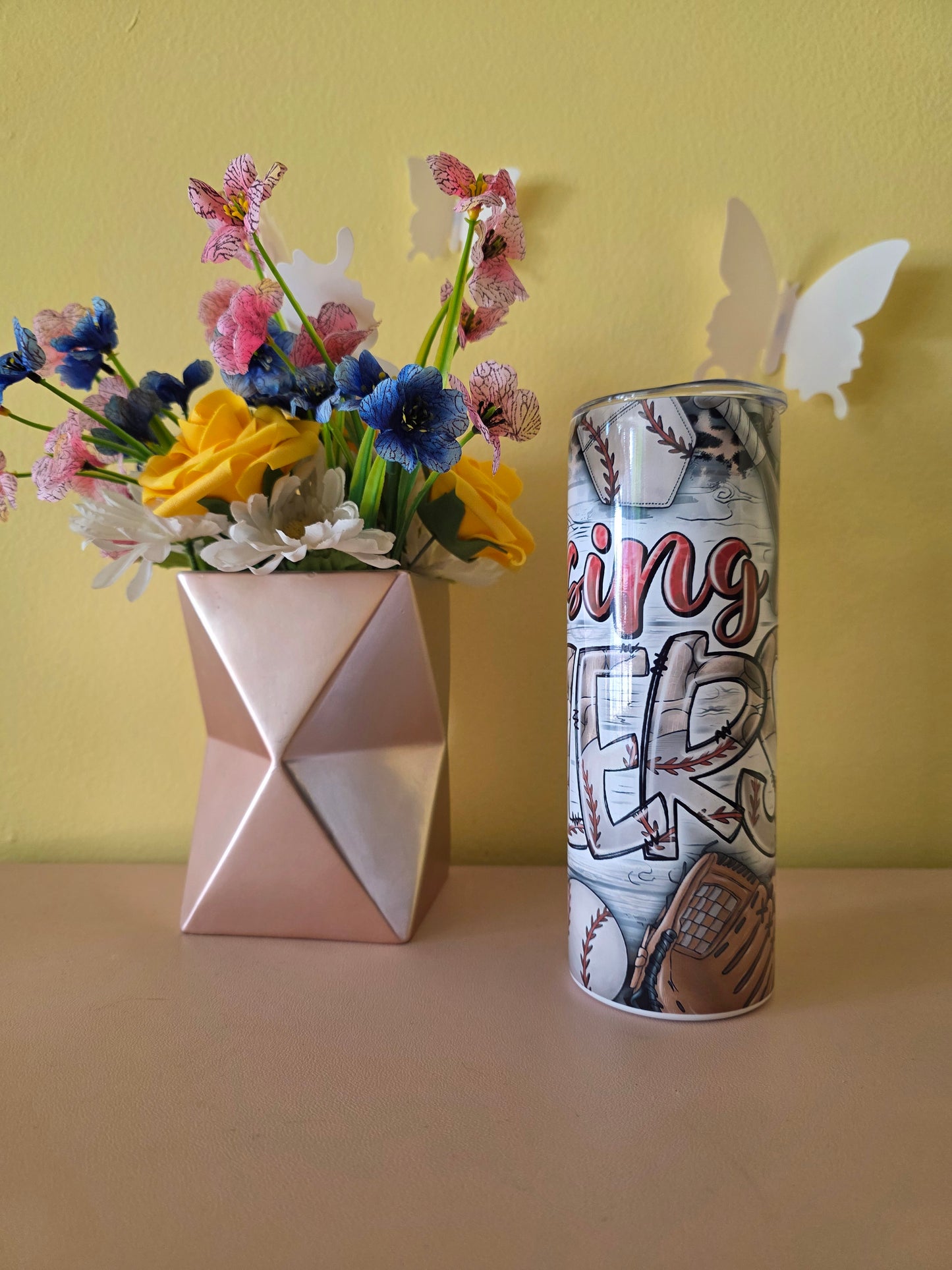 Decorative tumbler with colorful baseball design on a pink surface and yellow background