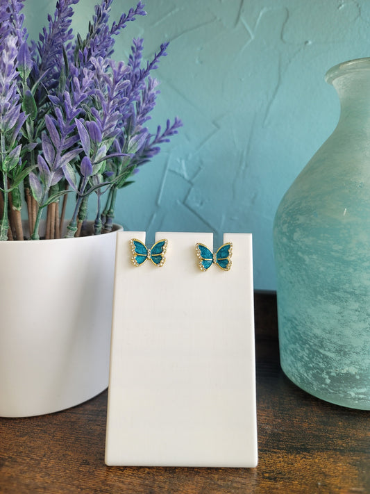Butterfly-shaped earrings on a white stand with a blurred natural background.