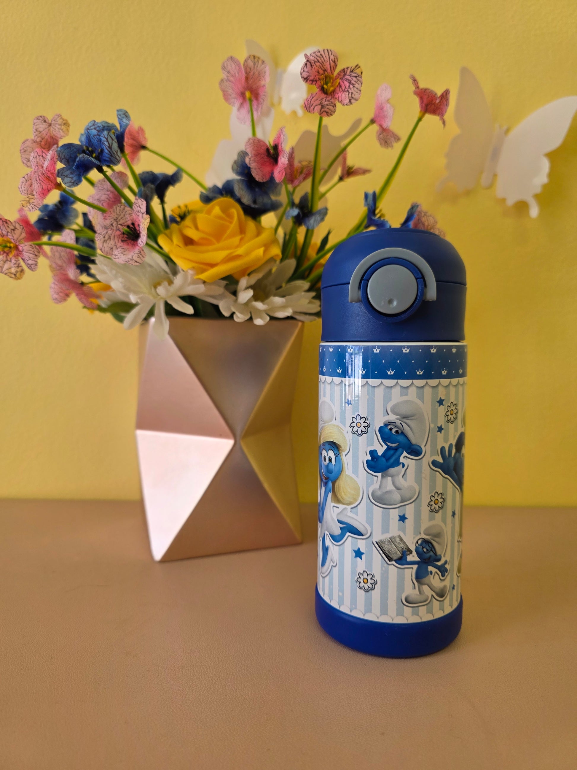Blue water bottle with cartoon design next to a bouquet of flowers on a yellow background