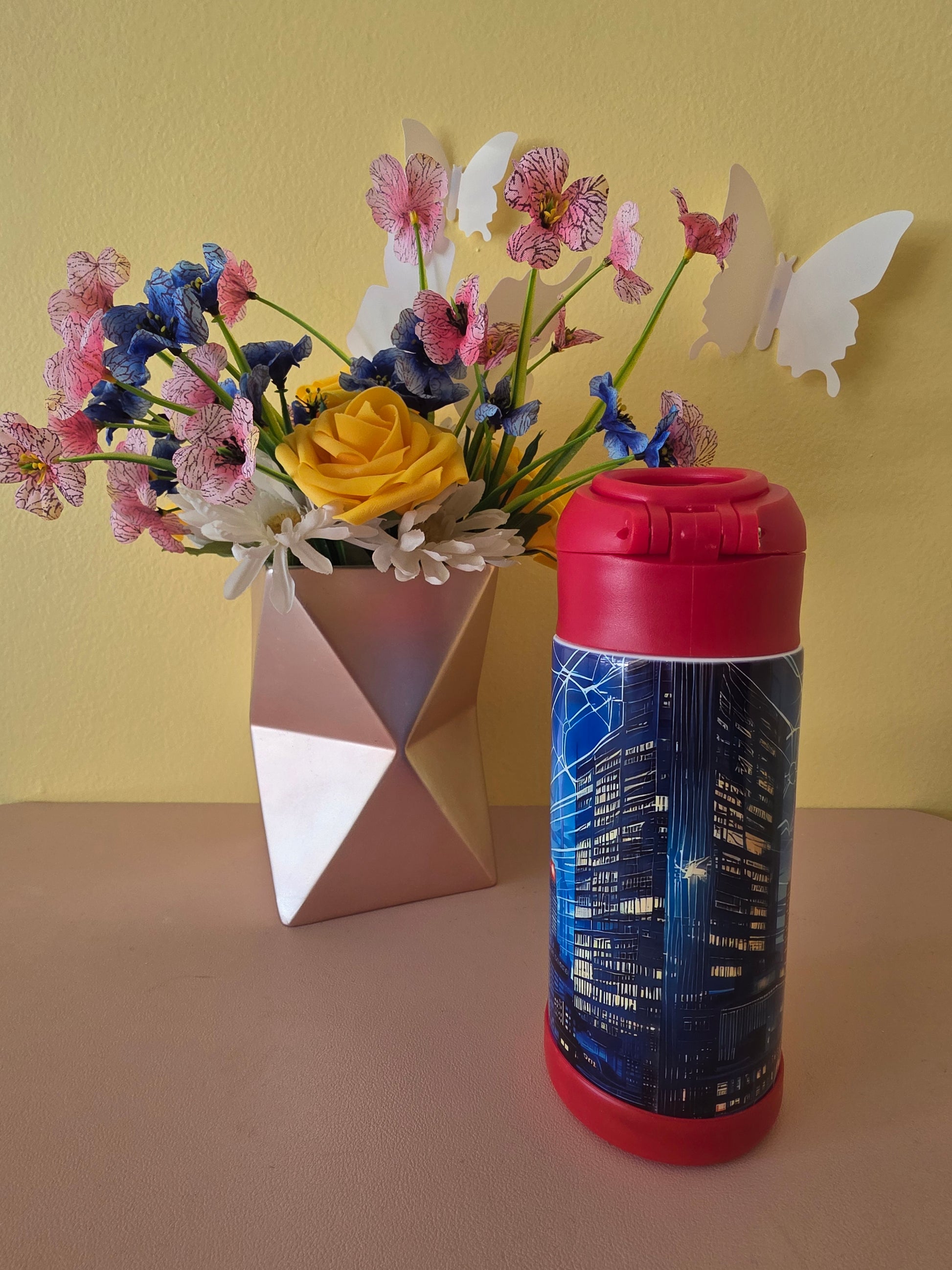 Spider-Man Superhero stainless steel water bottle for kids on a table with flowers in the background. 