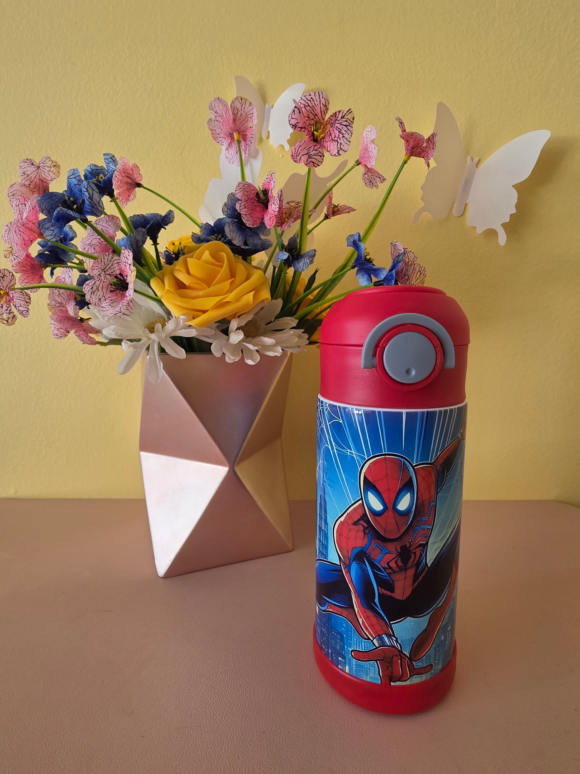 Spider-Man Superhero stainless steel water bottle for kids on a table with flowers in the background. 