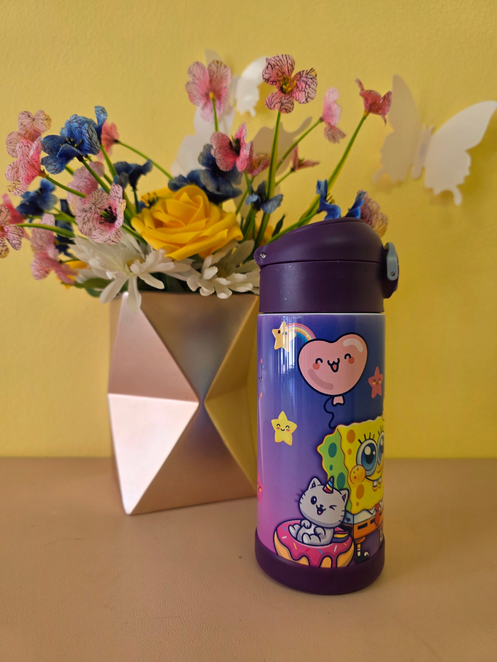 Colorful thermos with cartoon design on a yellow surface with flowers