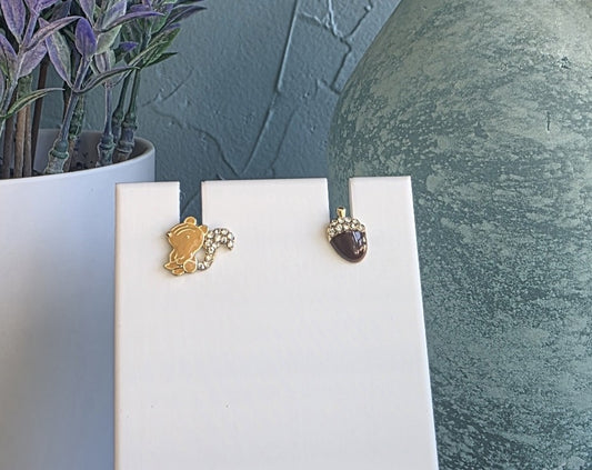 Two earrings on white stands with a plant and textured wall in the background