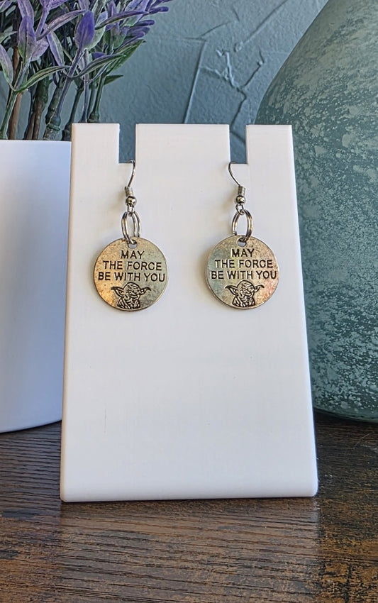 Silver 'May the Force Be With You' earrings on a white stand with a blurred background