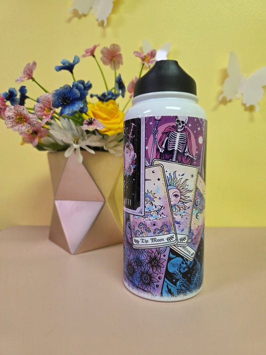 Tumbler with tarot card design on a yellow surface with flowers and geometric shapes.