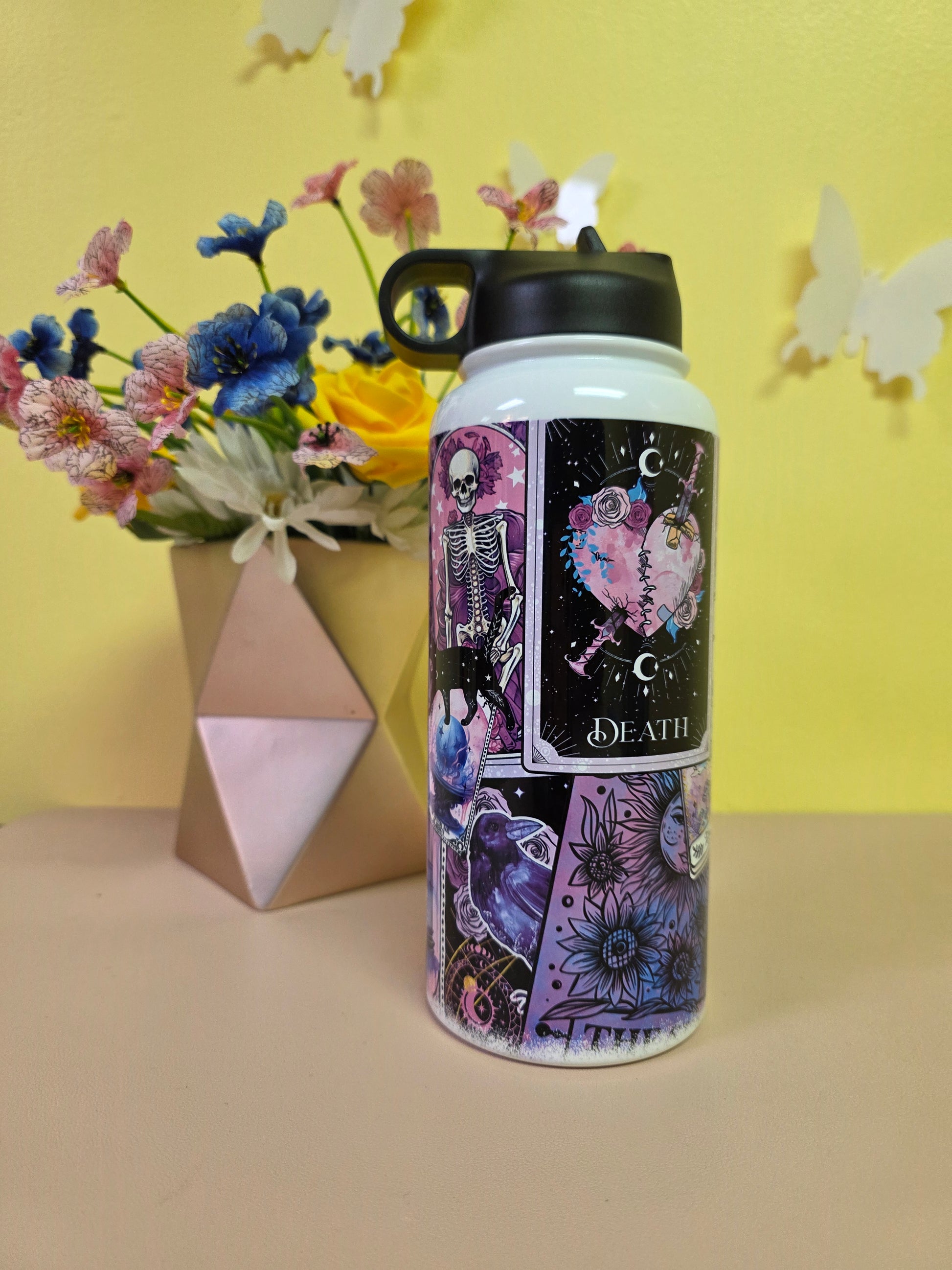 Tumbler with tarot card design on a yellow surface with flowers