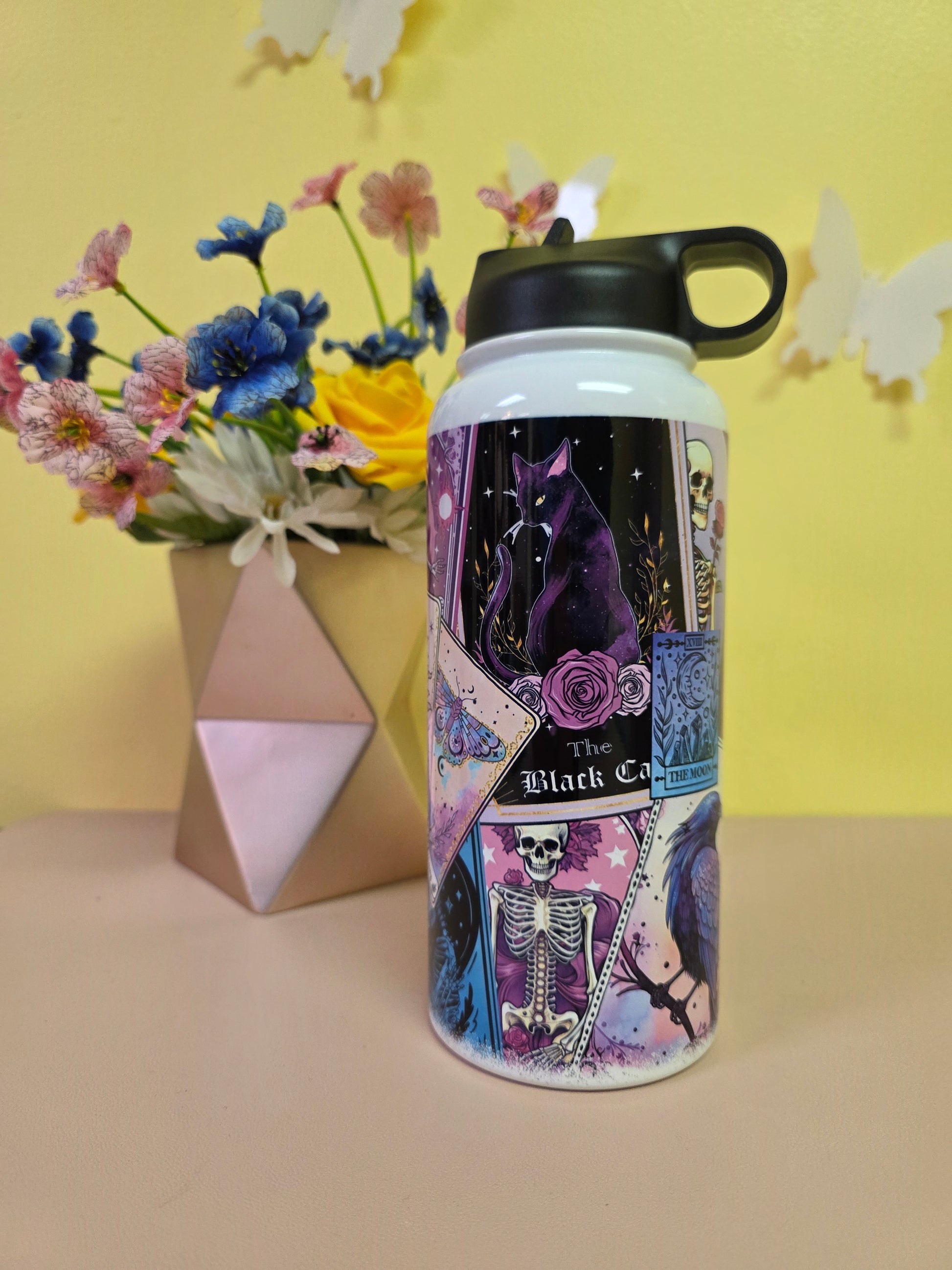 Colorful water bottle with a black handle on a yellow surface with flowers and a box.