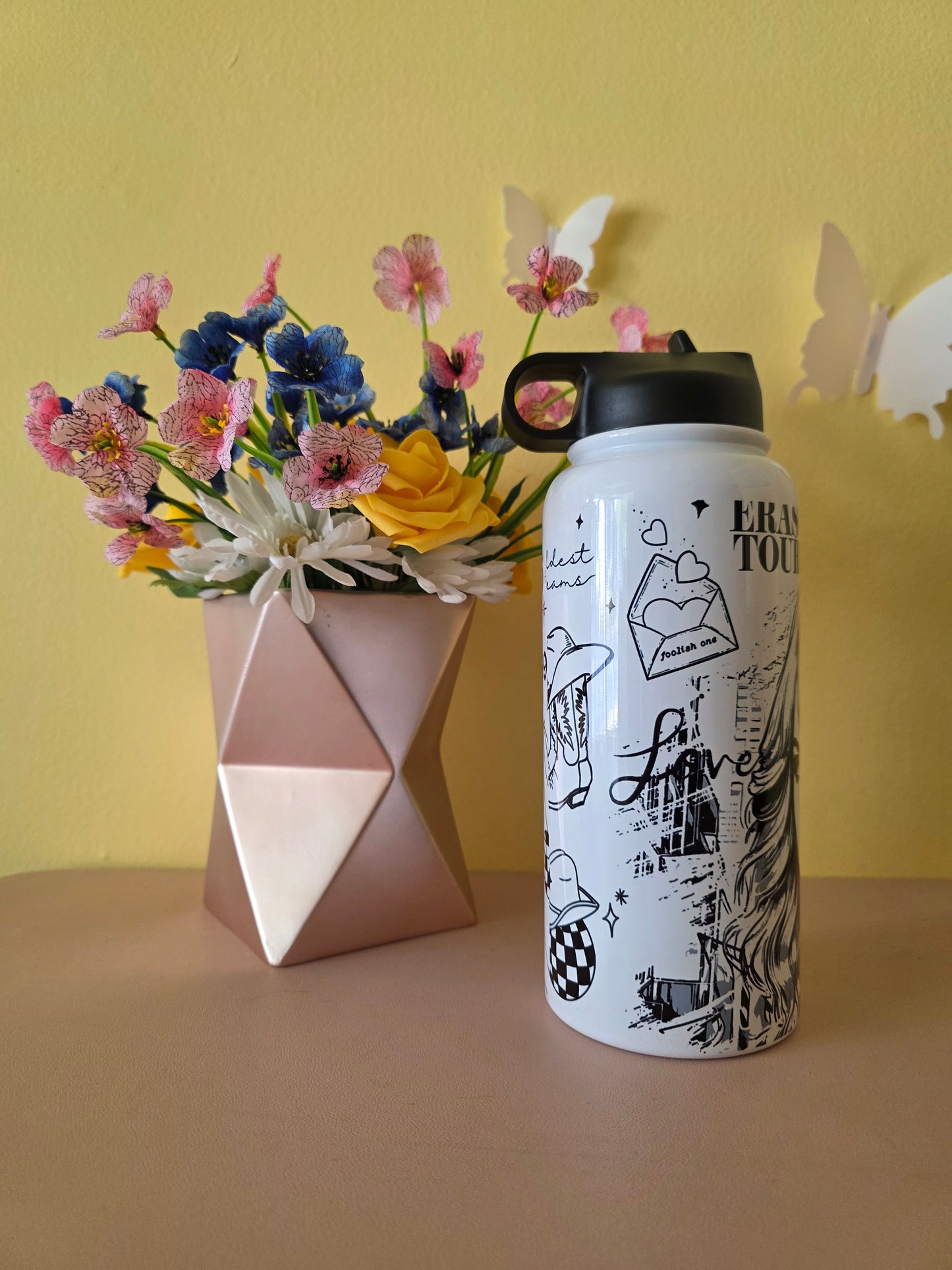 Taylor Swift themed water bottle tumbler on a table with a yellow background