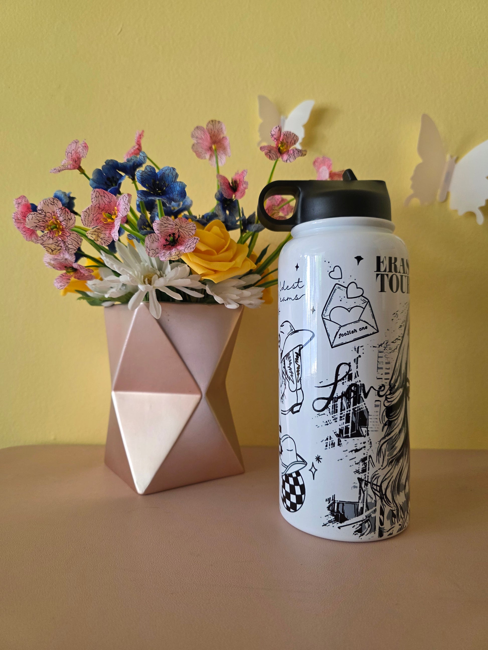 Taylor Swift themed water bottle tumbler on a table with a yellow background