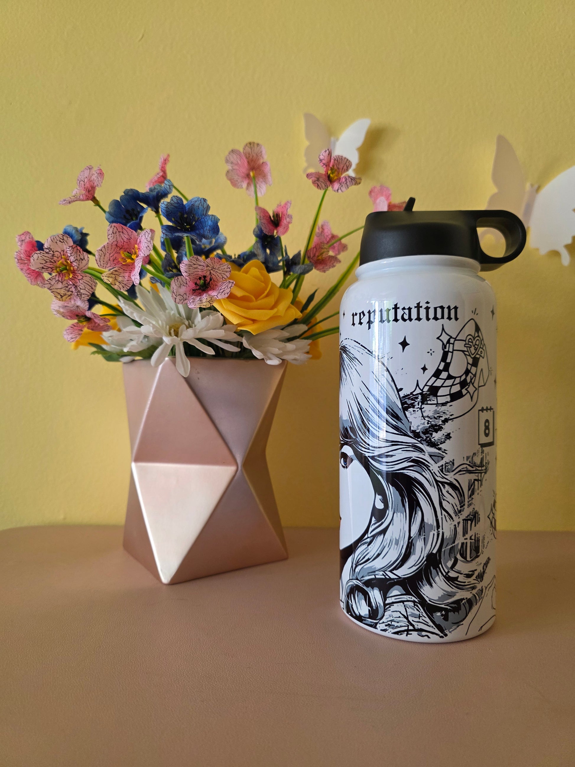 Taylor Swift themed water bottle tumbler on a table with a yellow background