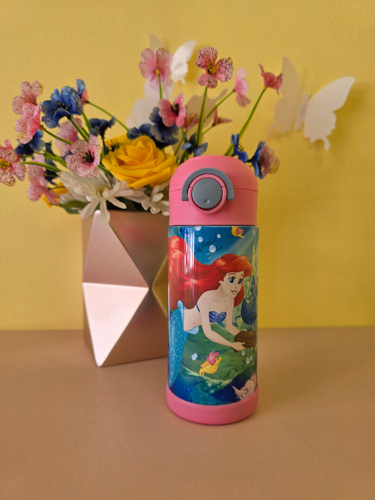 The Little Mermaid tumbler on a table with flowers on the background. 