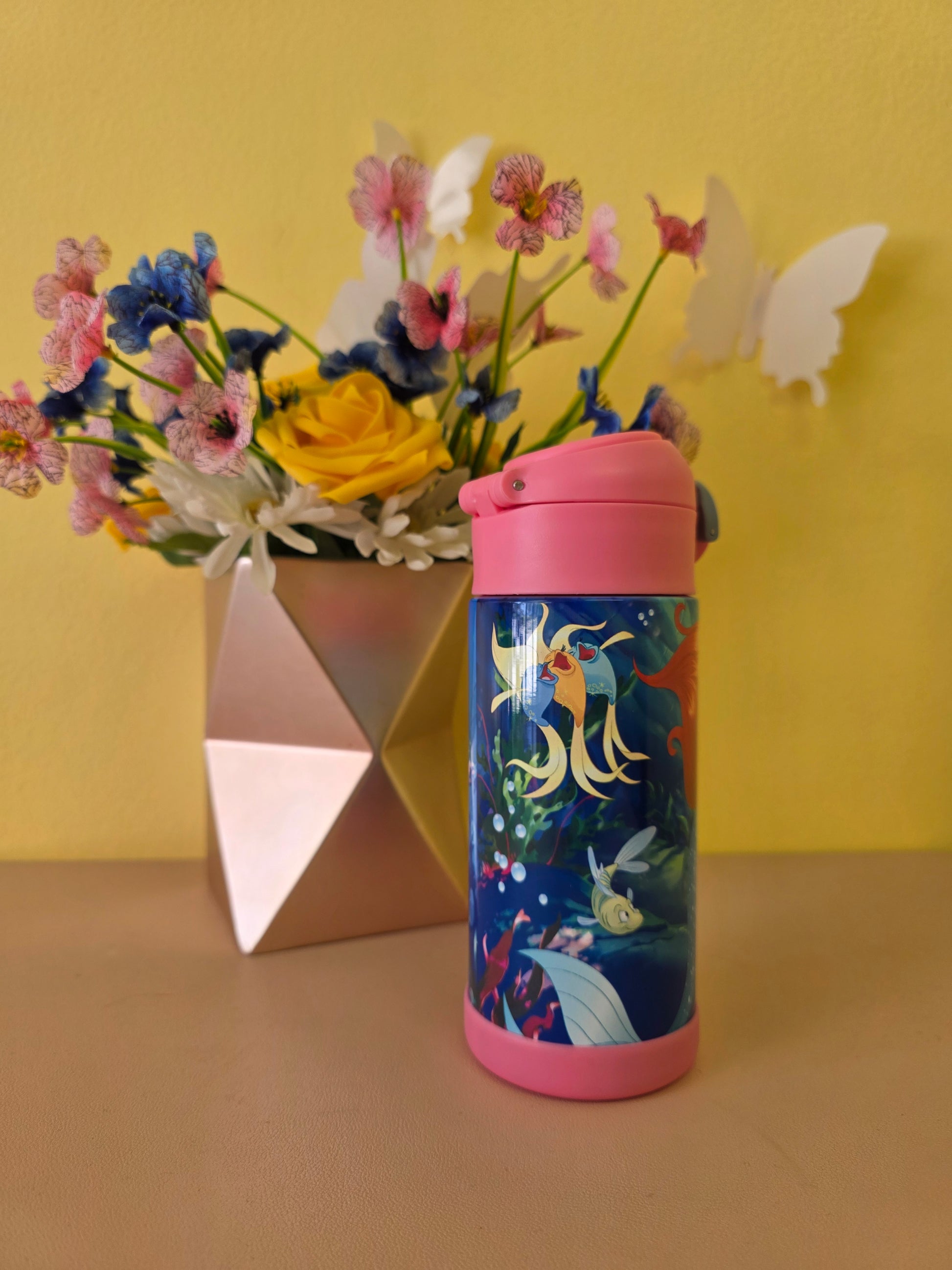 The Little Mermaid tumbler on a table with flowers on the background. 