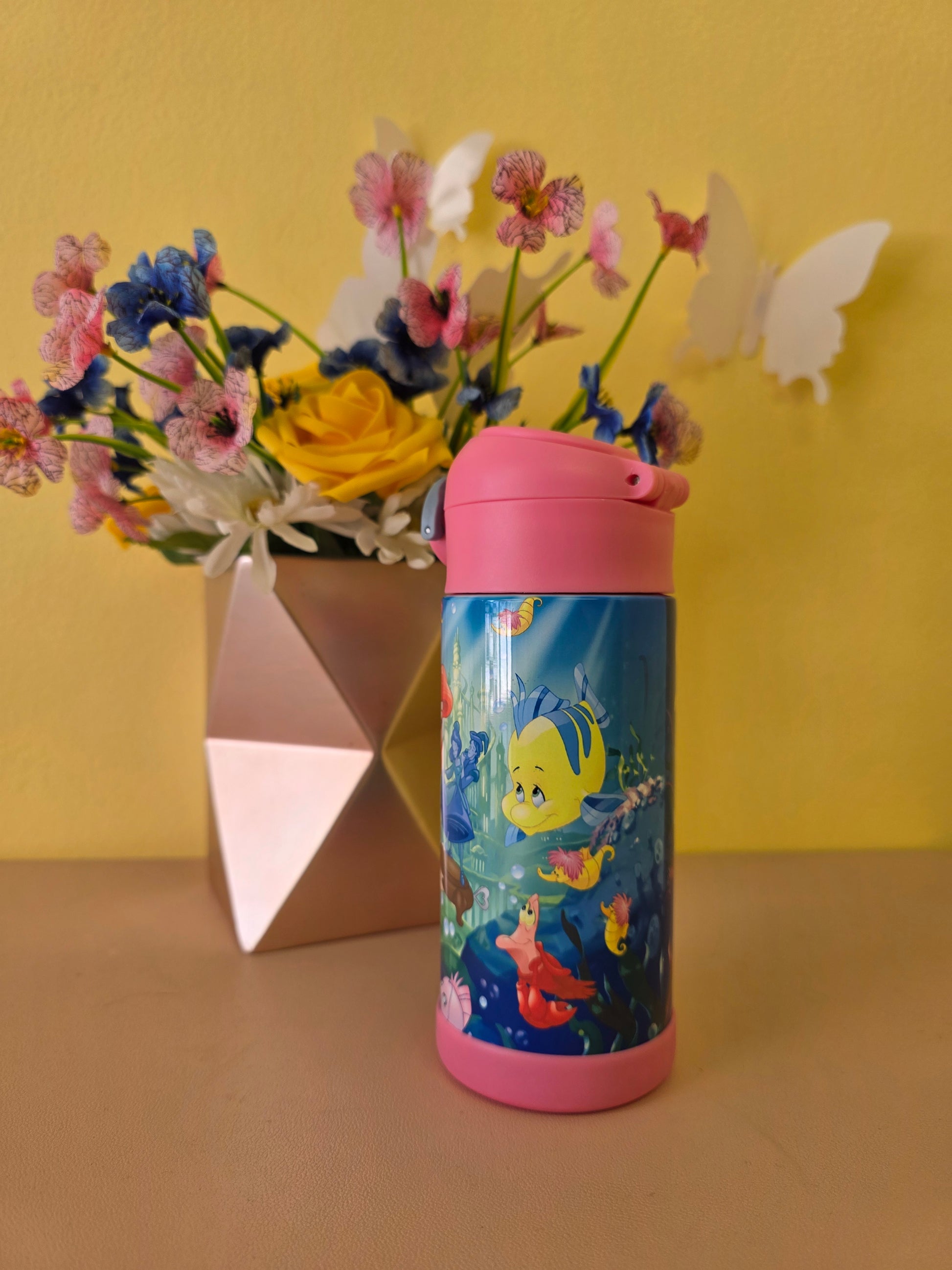 The Little Mermaid tumbler on a table with flowers on the background. 