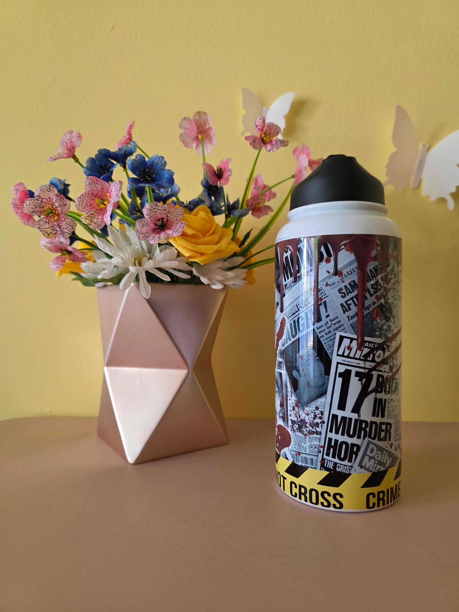 True Crime themed water bottle tumbler on a table with yellow background