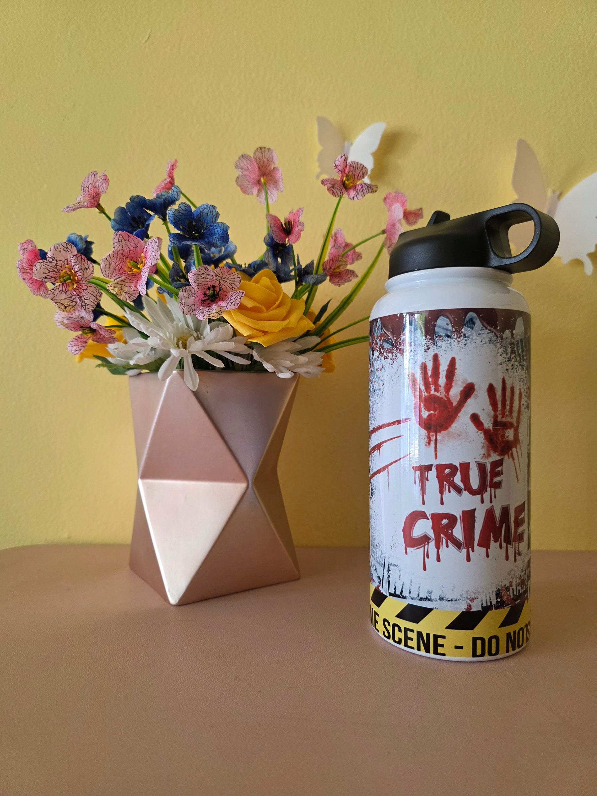 True Crime themed water bottle tumbler on a table with yellow background