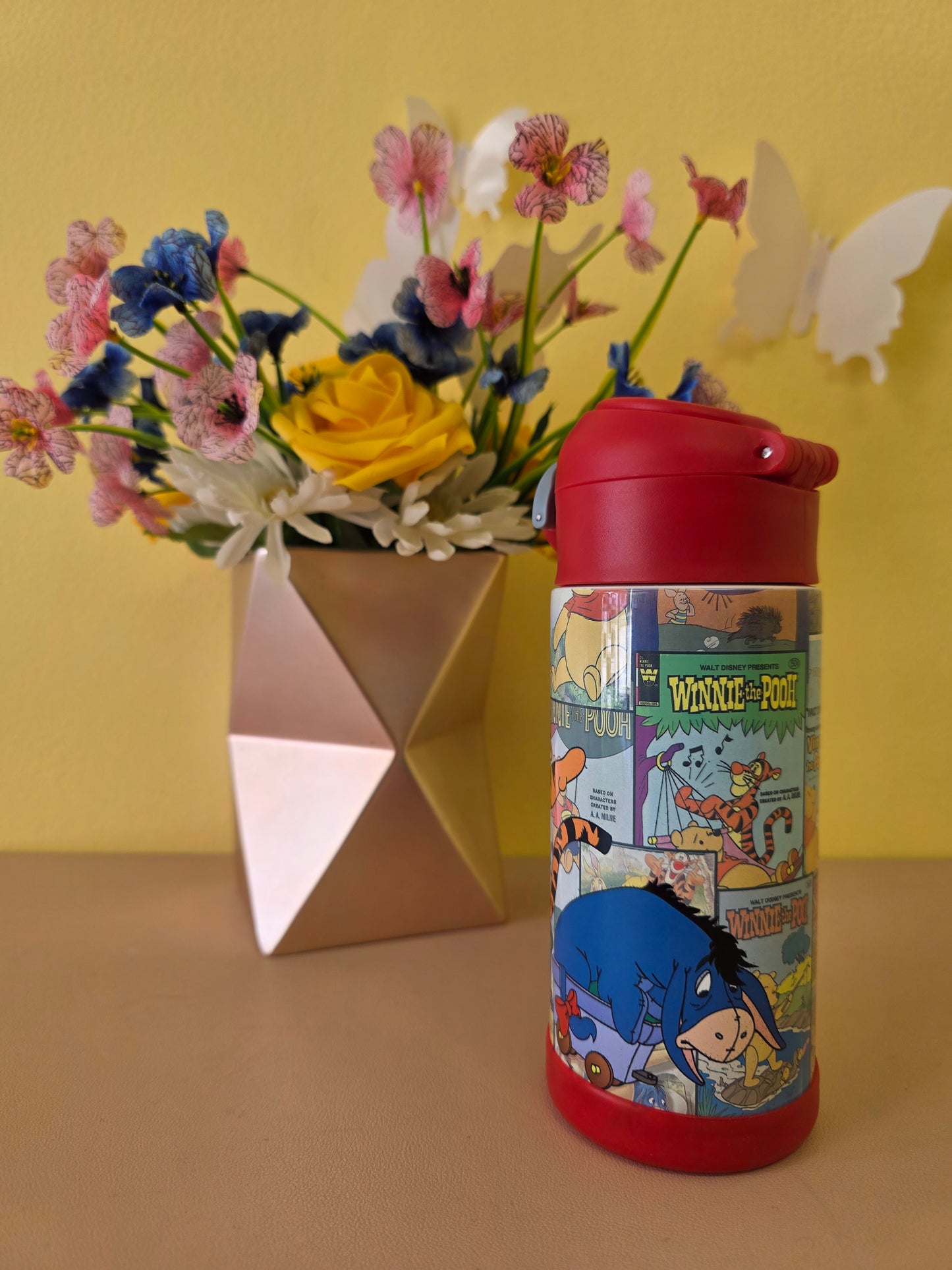 Winnie the Pooh tumbler on a table with flowers in the background. 