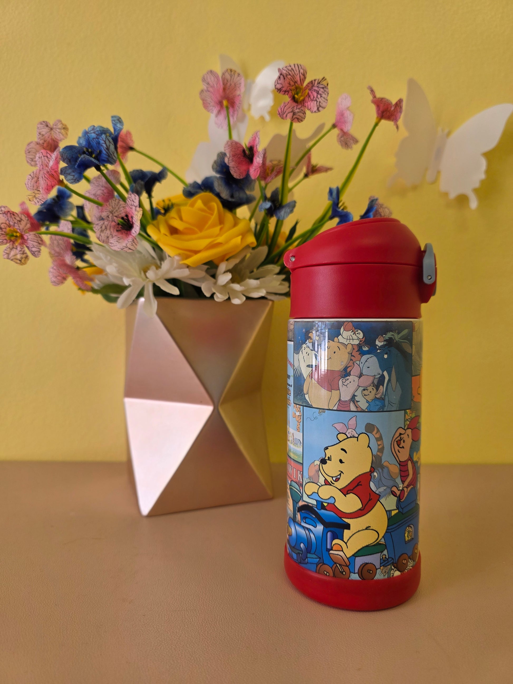 Winnie the Pooh tumbler on a table with flowers in the background. 