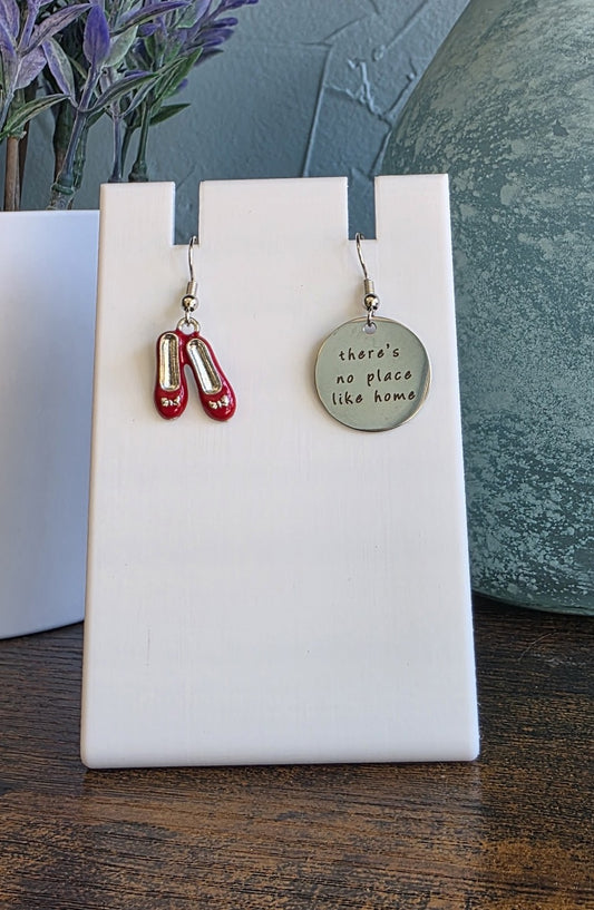 Pair of earrings on a white stand with a wooden surface and plant in the background