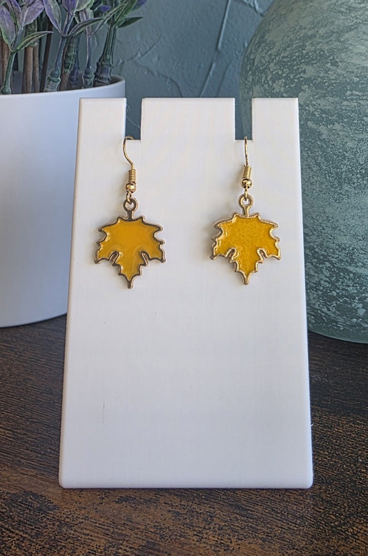 Gold leaf-shaped earrings on a white stand with a blurred background